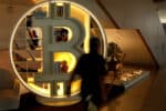 Bitcoin-Symbol in beleuchteter, moderner Umgebung mit Bücherregalen und Pflanzen.