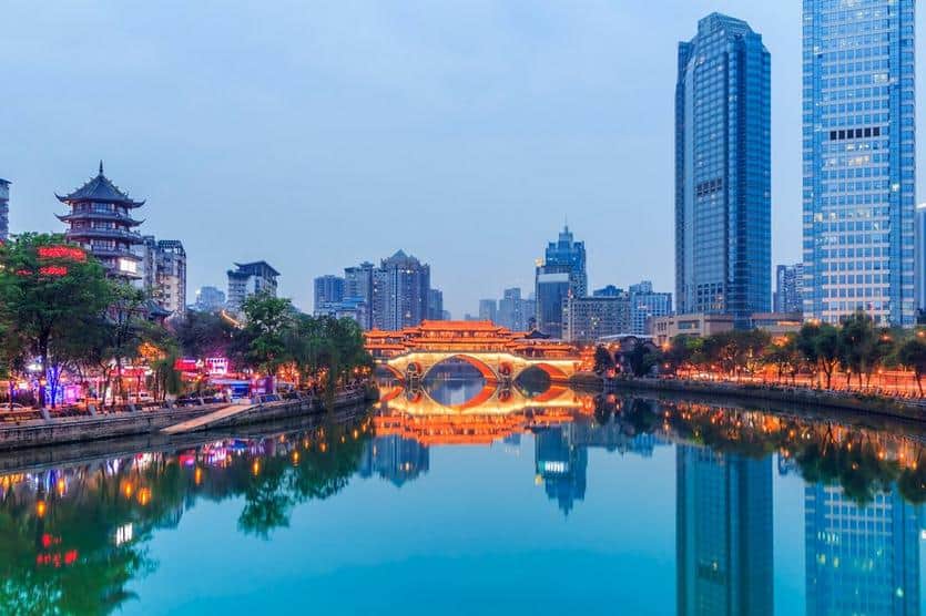 Hochhäuser und Brücke in einer modernen Stadt bei Nacht, reflektiert im Fluss.