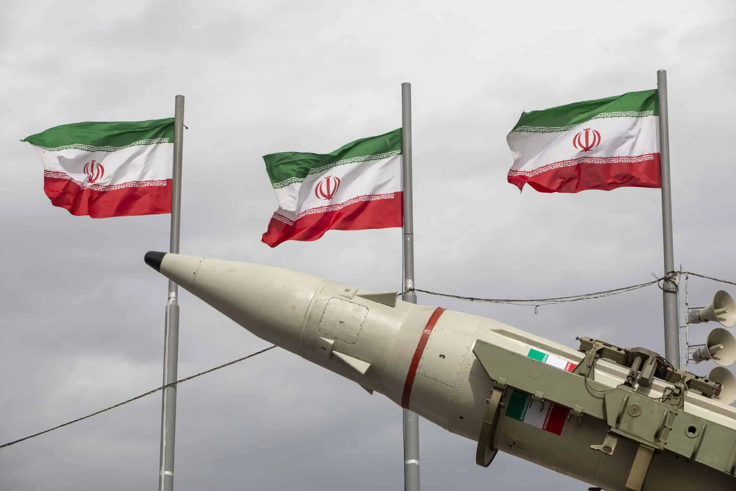 Iranische Flaggen wehen neben einer Rakete bei einer militärischen Demonstration.