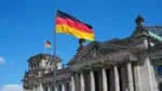 Reichstagsgebäude in Berlin mit Deutschlandflagge im Vordergrund.