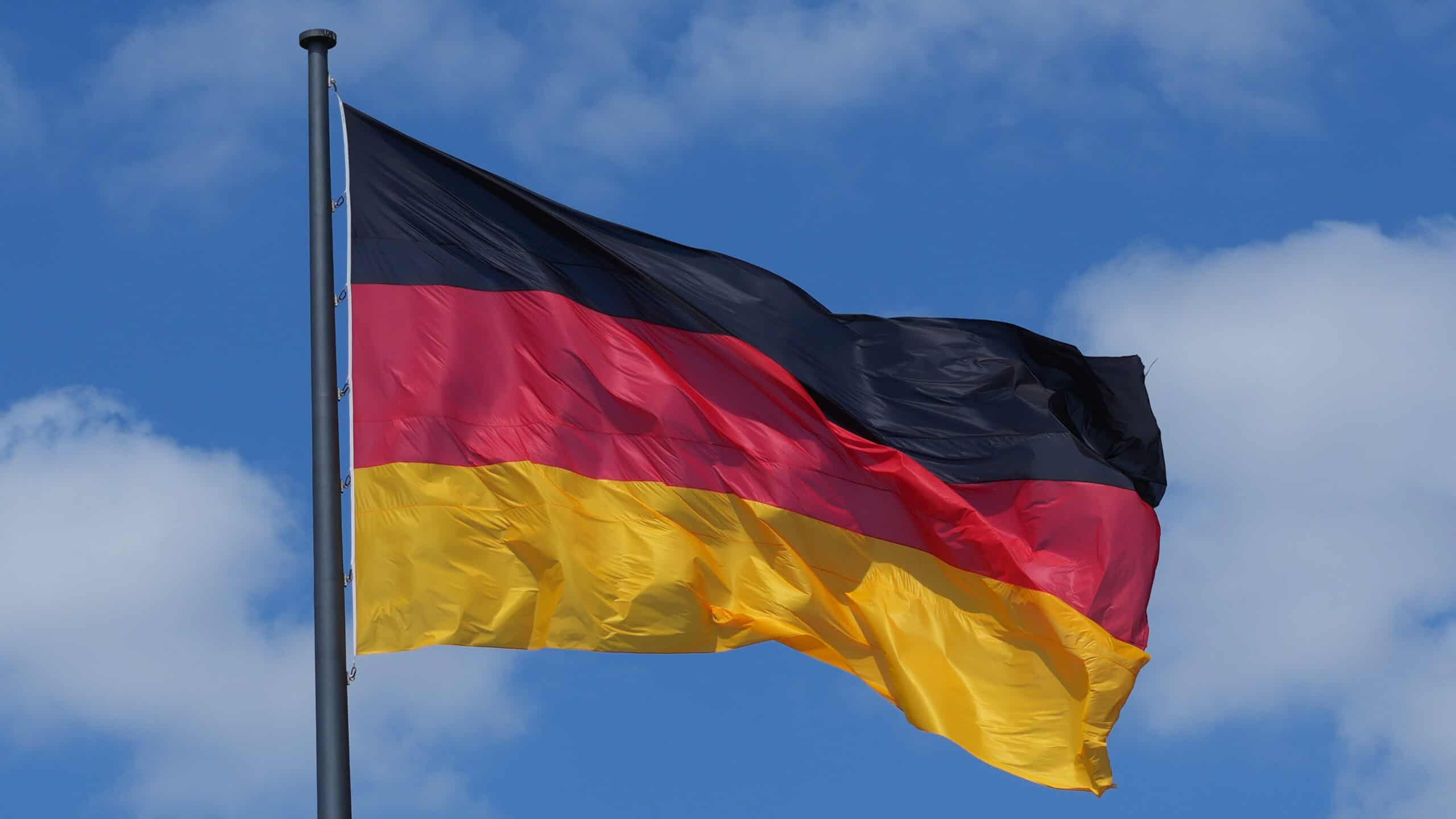 Deutsche Flagge weht im Wind vor blauem Himmel.