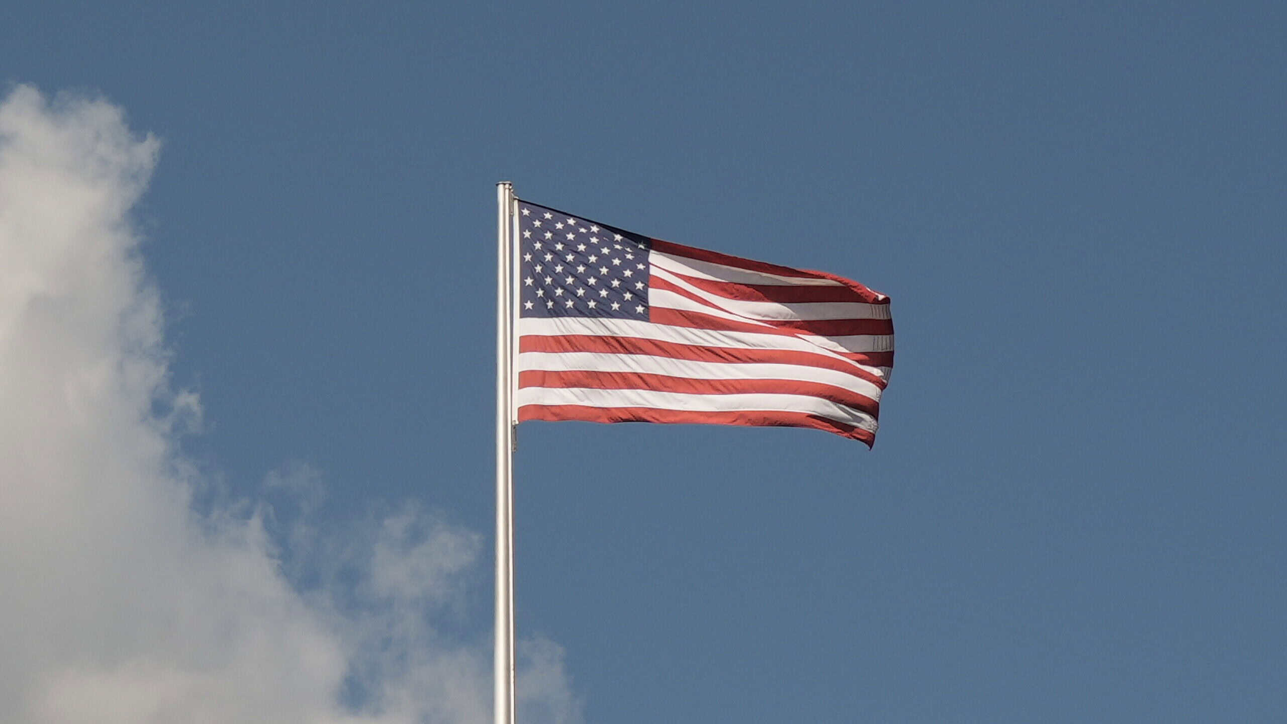 Amerikanische Flagge weht im Wind vor blauem Himmel.